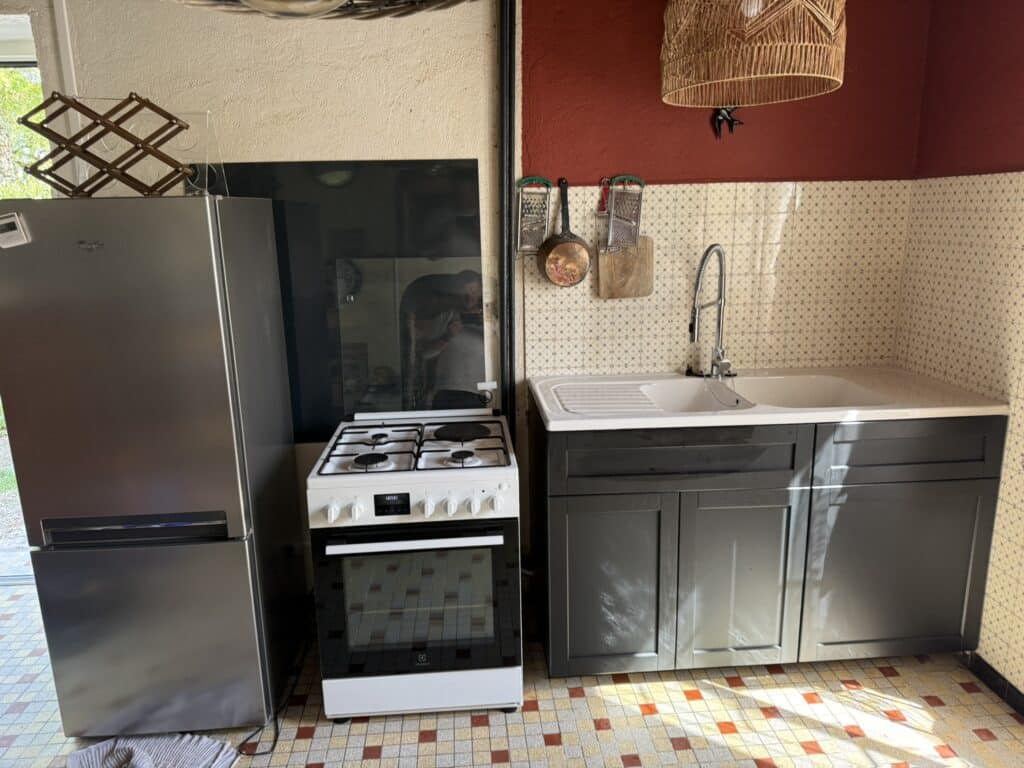 Cuisine avec réfrigérateur Whirlpool, cuisinière Electrolux (0:00), évier double, meubles gris foncé. Crédence à motifs, mur rouge, porte-bouteilles bois.