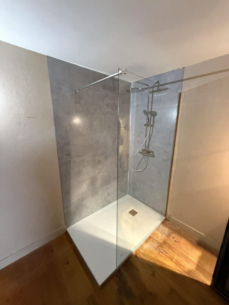 Cabine de douche à l'italienne moderne avec parois gris effet béton, receveur blanc, paroi vitrée et sol parquet en bois clair.